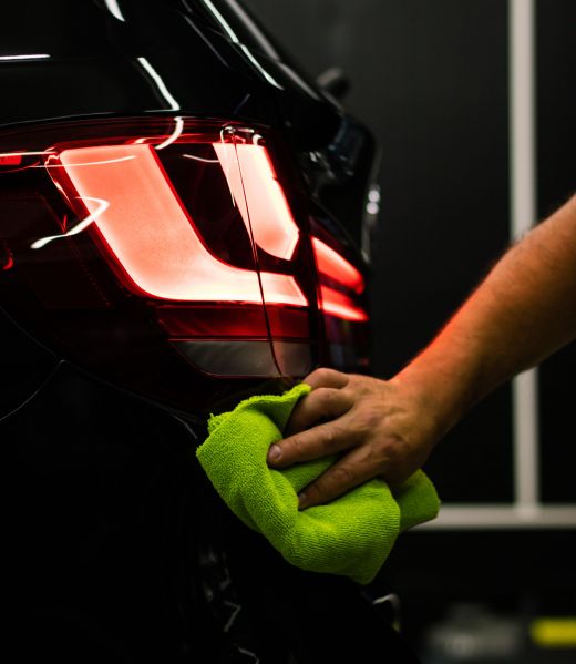 A selective focus shot of a man cleaning car's back headlight with a microfiber cloth